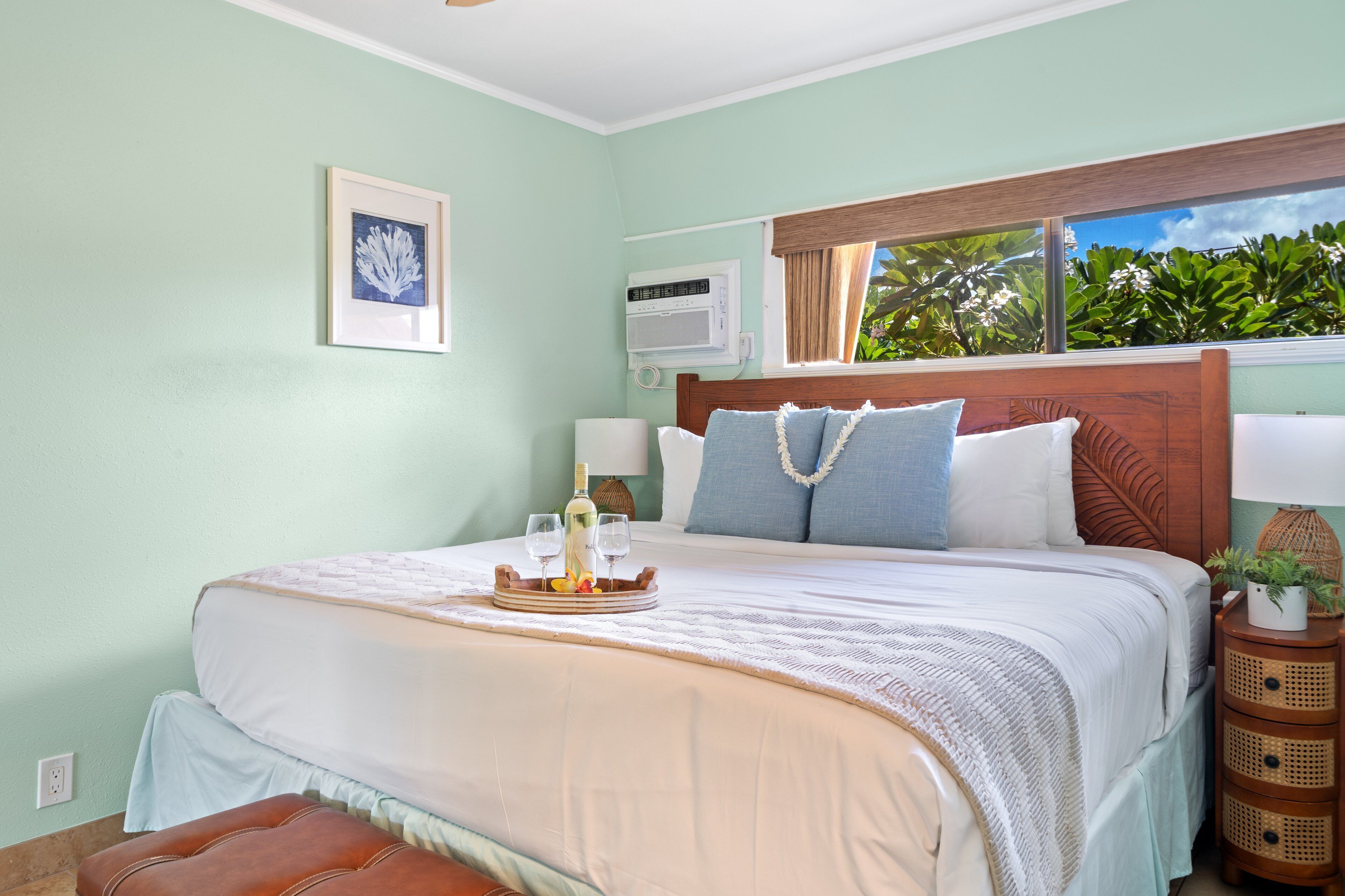 Une chambre à coucher bien rangée, avec un lit, des tables de chevet, une fenêtre donnant sur un paysage verdoyant et un tableau encadré au mur.
