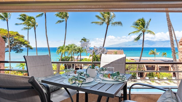 Un comedor con una mesa para dos, con vista a una playa con palmeras y el océano.