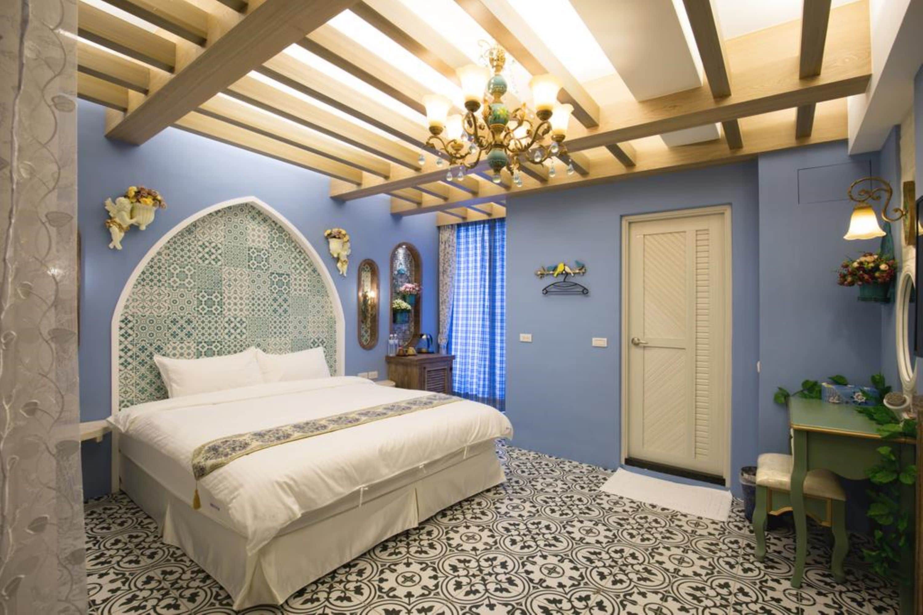 Un dormitorio con una cama grande, una araña, techo de madera y baldosas de suelo con diseño.
