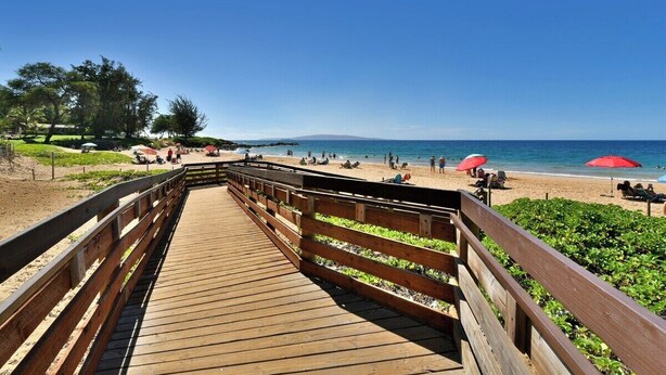 A wooden boardwalk leading to a beach with umbrellas and people. - Cozy Condo Near Beach w Ocean View Pool - Kihei Akahi C616 (Kihei)