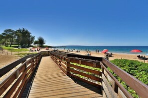 A wooden boardwalk leading to a beach with umbrellas and people.