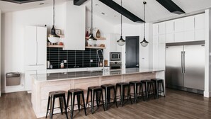 Una cocina moderna con una isla central, taburetes de bar, electrodomésticos de acero inoxidable e iluminación colgante.