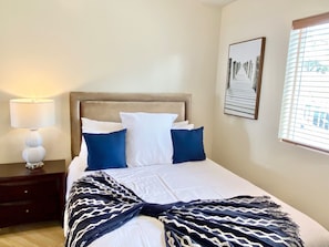 Una cama bien tendida con un plaid estampado, una lámpara de noche y un cuadro en la pared.