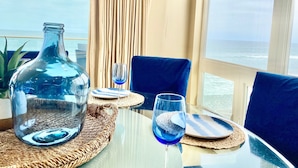 A table set for two with a view of the ocean, a large glass bottle, and blue glassware. - 5 BR Large Beach House, Beachfront with Fire Ring,  Walk to Restaurants (Oceanside)