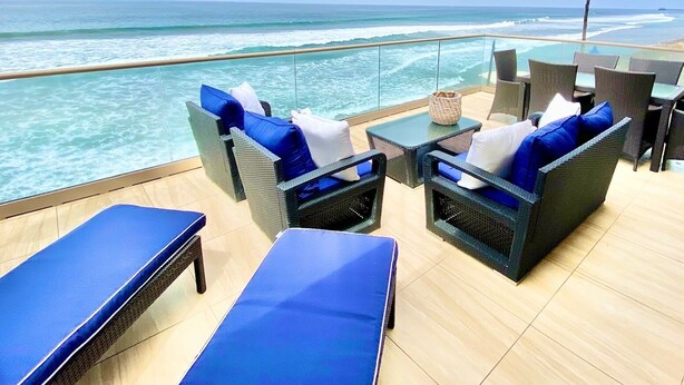 A balcony with wicker furniture and blue cushions, overlooking the ocean. - 5 BR Large Beach House, Beachfront with Fire Ring,  Walk to Restaurants (Oceanside)