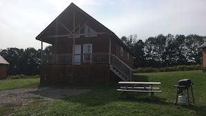 Eine zweistöckige Holzhütte mit Balkon, Picknicktisch und Grill.