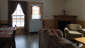 Ein gemütliches Zimmer mit Holzbalkendecke, Kamin, einer Couch, einem Tisch und einer mit Vorhängen versehenen Tür.