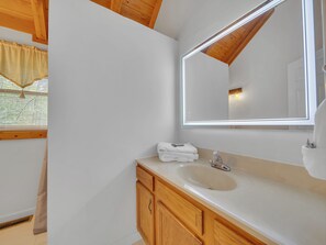 Un baño con lavamanos blanco, armarios de madera y un espejo grande.