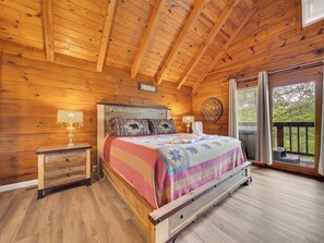 A wooden cabin bedroom with a bed, two bedside tables, and a window with a view of trees.