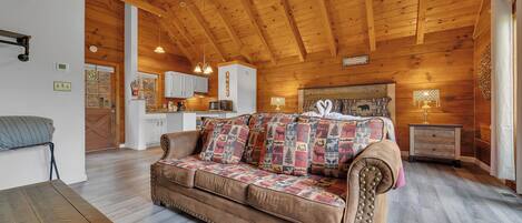 Interior acogedor de una cabaña con techo de madera, un sofá marrón con cojines estampados, una mesa de comedor y una zona de cocina.