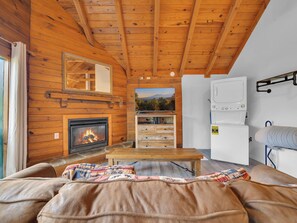 A cozy cabin interior with a fireplace, wooden walls, a television, and a bed.