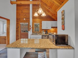 A kitchen with granite countertops, wooden cabinets, a built-in microwave, and a hanging light fixture.