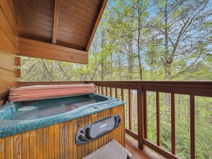 Una terraza de madera con un jacuzzi, barandas de madera y vistas a un bosque.