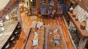 Un acogedor espacio tipo loft con chimenea de piedra, vigas de madera y pared de piedra. Ofrece múltiples opciones de asiento, incluyendo un sofá, sillas y una zona de bar con taburetes.