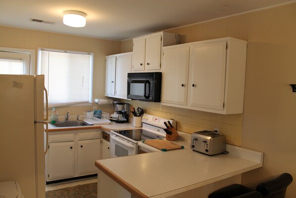 Una cocina compacta con armarios blancos, microondas, tostadora y electrodomésticos básicos.