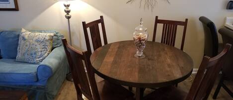 A dining area with a wooden table, four chairs, a decorative mirror, a lamp, and a blue sofa with a patterned pillow.