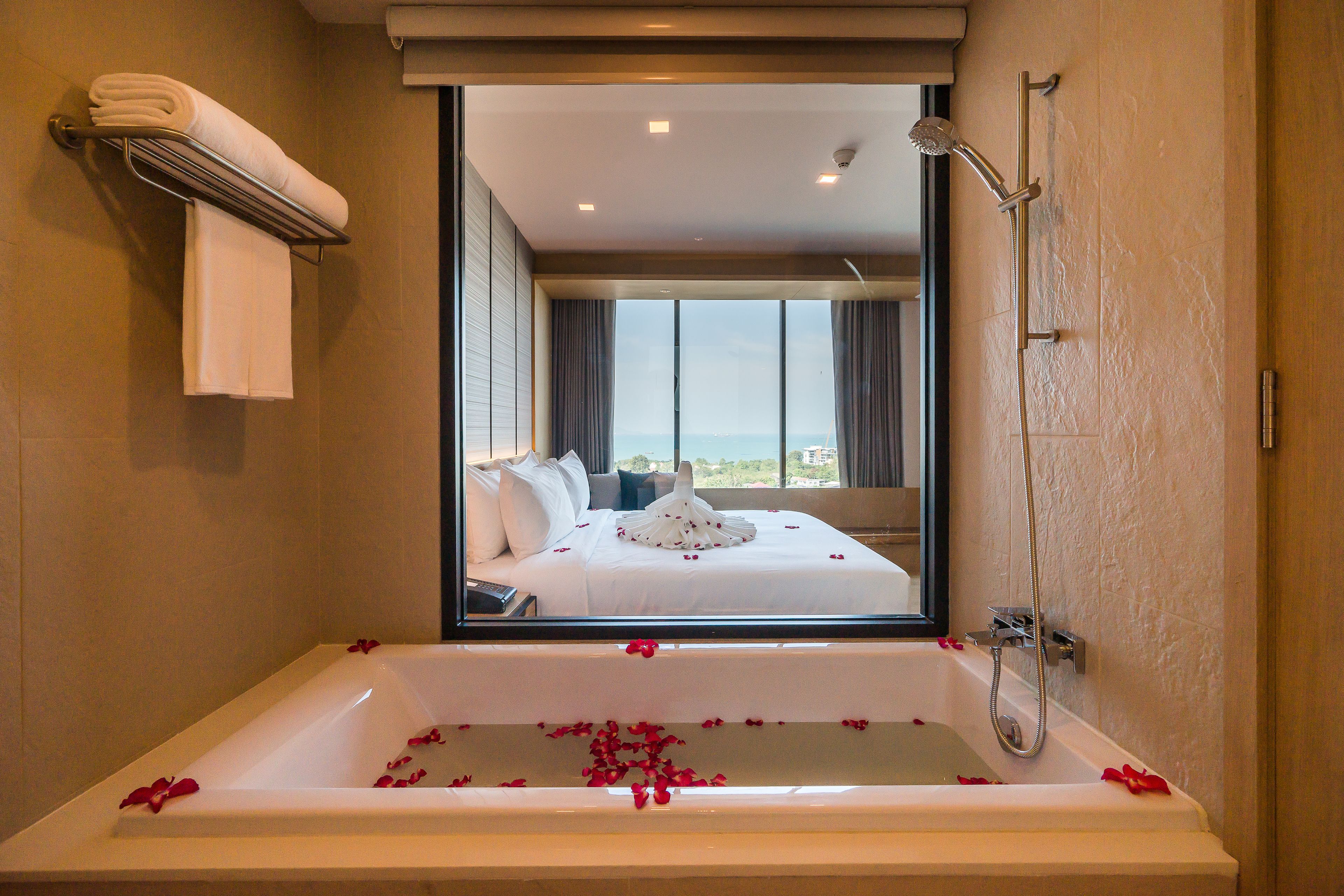 A modern bathroom with a large bathtub, a shower, and a view of a bedroom with a bed and a balcony.