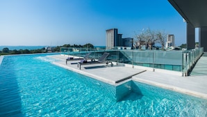 Une piscine à débordement située sur le toit, avec des chaises longues, une balustrade en verre et une vue imprenable sur les toits de la ville.