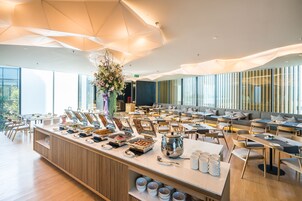 Un comedor moderno con una barra libre, disposición de mesas y amplias ventanas que dejan entrar luz natural.