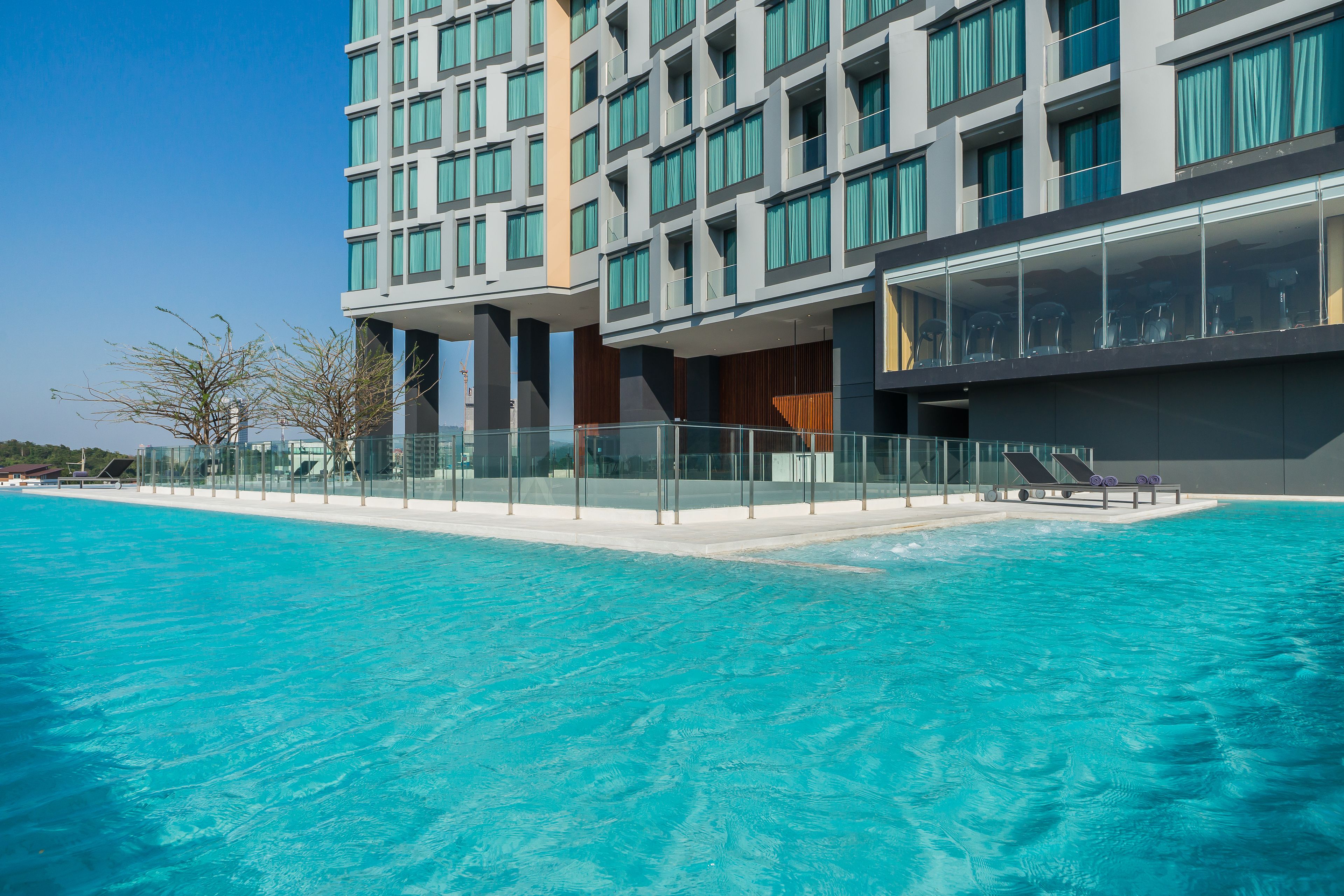 A modern hotel with a swimming pool, glass railings, and a view of the building's exterior.