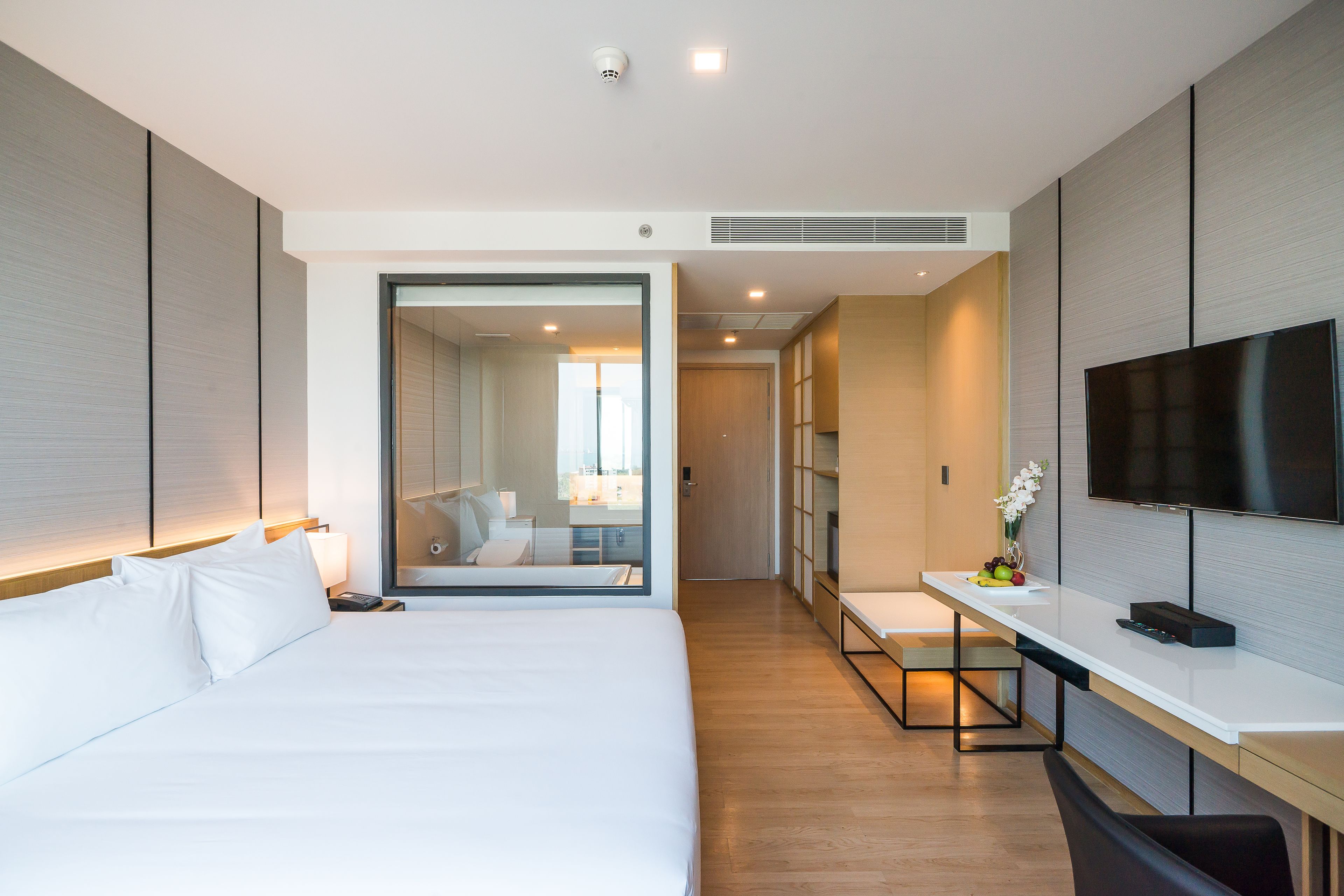 Una habitación de hotel moderna con una cama grande, un escritorio con televisor de pantalla plana y vistas al baño contiguo.