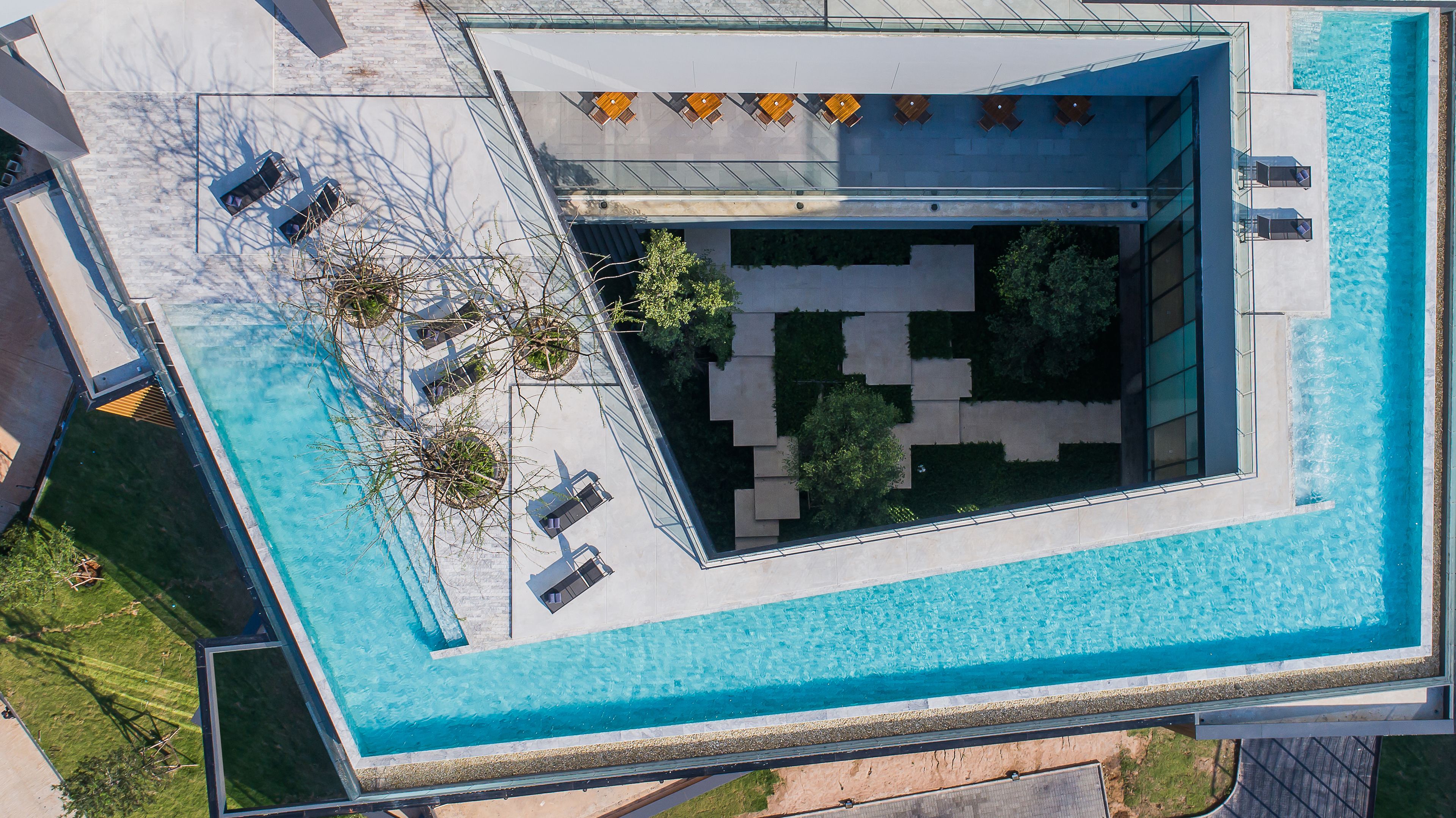 Luchtbeeld van een modern gebouw met een rechthoekig zwembad, buitenzitplaatsen en een aangelegde tuin.