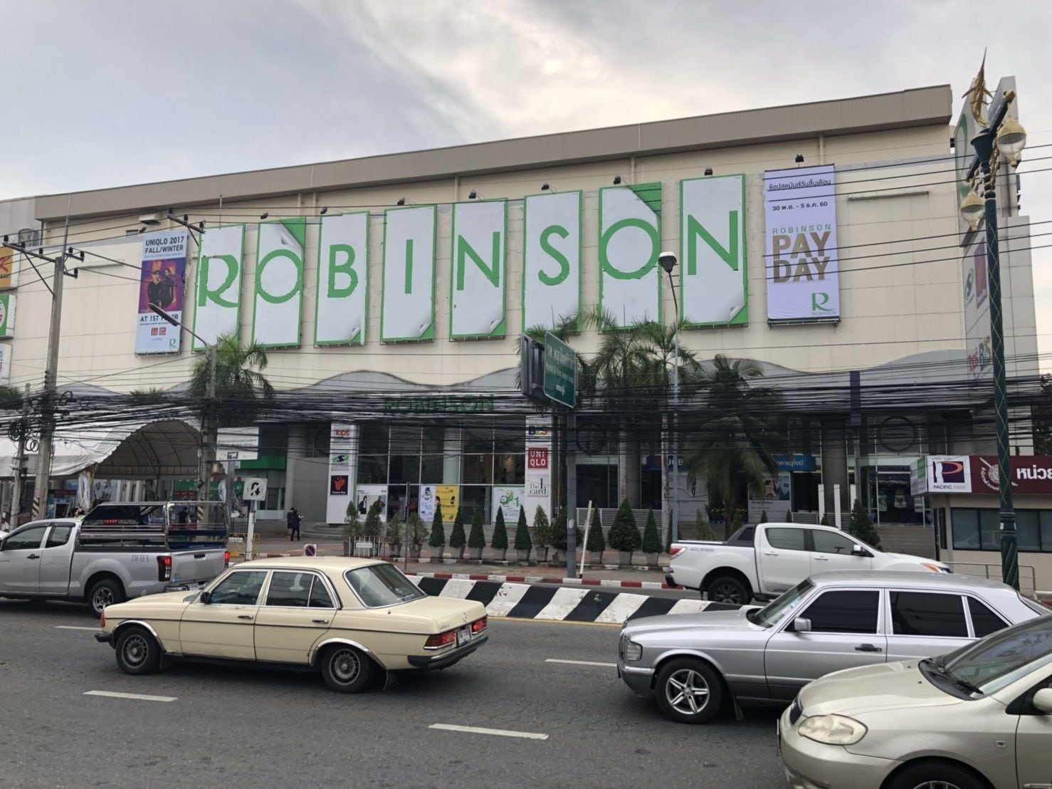 Una tienda Robinson Pay R con un cartel grande, varios pendones y un estacionamiento con varios autos.