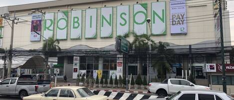 Una tienda Robinson Pay R con un cartel grande, varios pendones y un estacionamiento con varios autos.