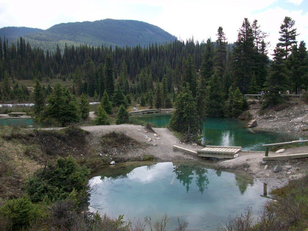 A natural landscape with a lake, surrounded by dense forest and mountains in the background.