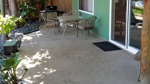 Un espace extérieur aménagé en terrasse, avec une table et des chaises, entouré de plantes et comprenant un barbecue.