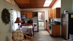 Une cuisine compacte avec des meubles en bois, un four à micro-ondes, une cuisinière et un réfrigérateur. On y trouve un coin repas avec une table et des chaises, et une vue sur l’extérieur par une porte.