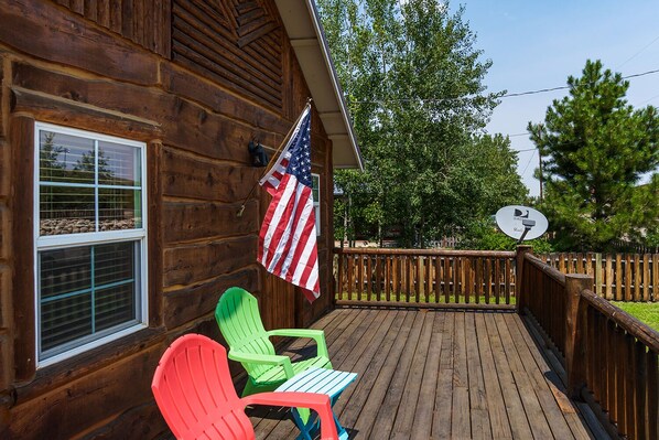 A wooden deck with a satellite dish, an American flag, and colorful Adirondack chairs.