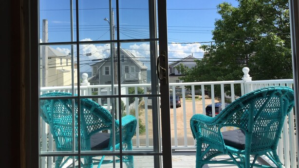 A view from a window with a white railing, overlooking a street with houses and a clear sky.
