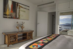 A bedroom with a large bed, a wooden console table with decorative items, a colorful quilt, and a view of the outdoors through a large window. - 3 Bedroom Sea View Sunset Apartment SDV120-By Samui Dream Villas (Koh Samui)