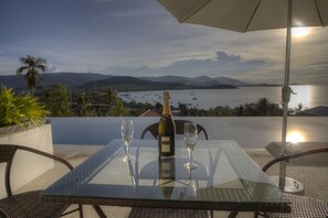 A table with a bottle of champagne and two glasses, overlooking a scenic bay with boats and mountains. - 3 Bedroom Sea View Sunset Apartment SDV120-By Samui Dream Villas (Koh Samui)