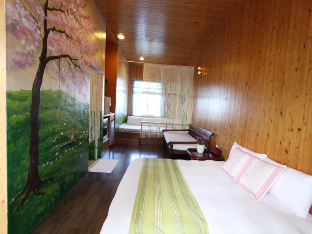 A room with a bed, a bench, a window, and a mural of a tree.
