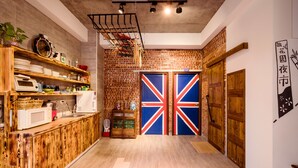 A kitchen with wooden cabinets, a microwave, and a hanging rack. There is a door with a Union Jack design and a sign with Chinese characters. - Anping 156 B&B (Tainan)