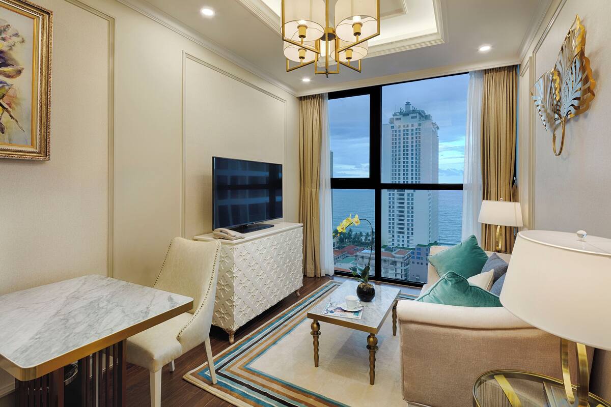 Quarto de hotel moderno com uma grande janela, televisão de tela plana, mesa de jantar, sofá e abajur decorativo.