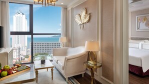 A hotel room with a large window offering a city view, a sofa, a bedside table with a lamp, and a bed with a headboard. - Vinpearl Empire Nha Trang, Affiliated by Meliá (Nha Trang)