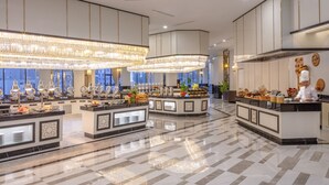 Un amplio vestíbulo de hotel con varias estaciones de buffet, elegantes candelabros y un chef preparando comida.