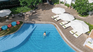 Vue aérienne d’un espace piscine avec des chaises longues et des parasols, entouré de verdure et bordé d’une allée dallée.