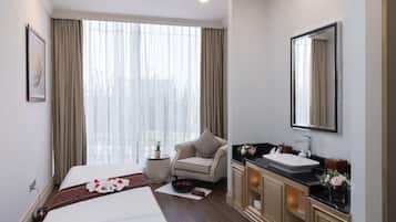 A hotel room with a bed, a sitting area with a chair, a vanity with a mirror, and a window with curtains.