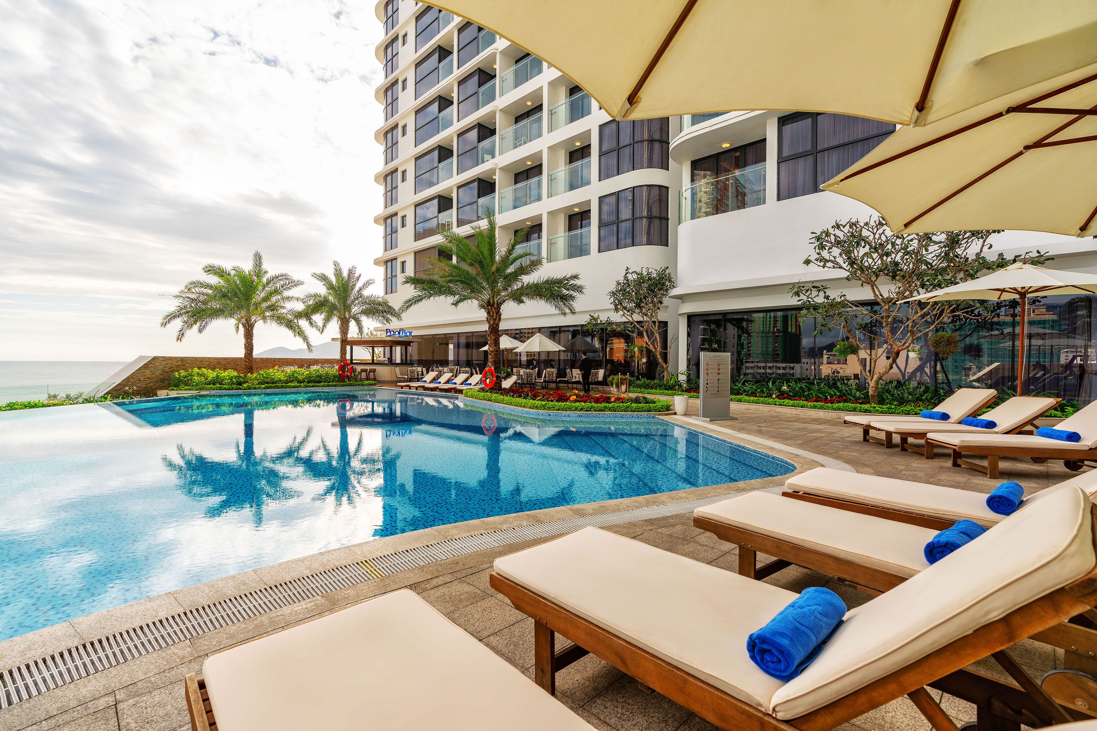 Un espace piscine d’hôtel avec des chaises longues et des parasols, une piscine à eau claire et une vue sur l’océan.