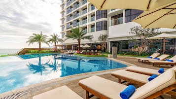 A hotel pool area with lounge chairs and umbrellas, a clear pool, and a view of the ocean.