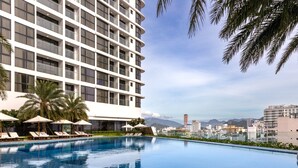 Un hotel moderno con una piscina grande, tumbonas y palmeras.