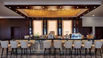 Una zona de bar con una barra larga, varios taburetes y un moderno candelabro.
