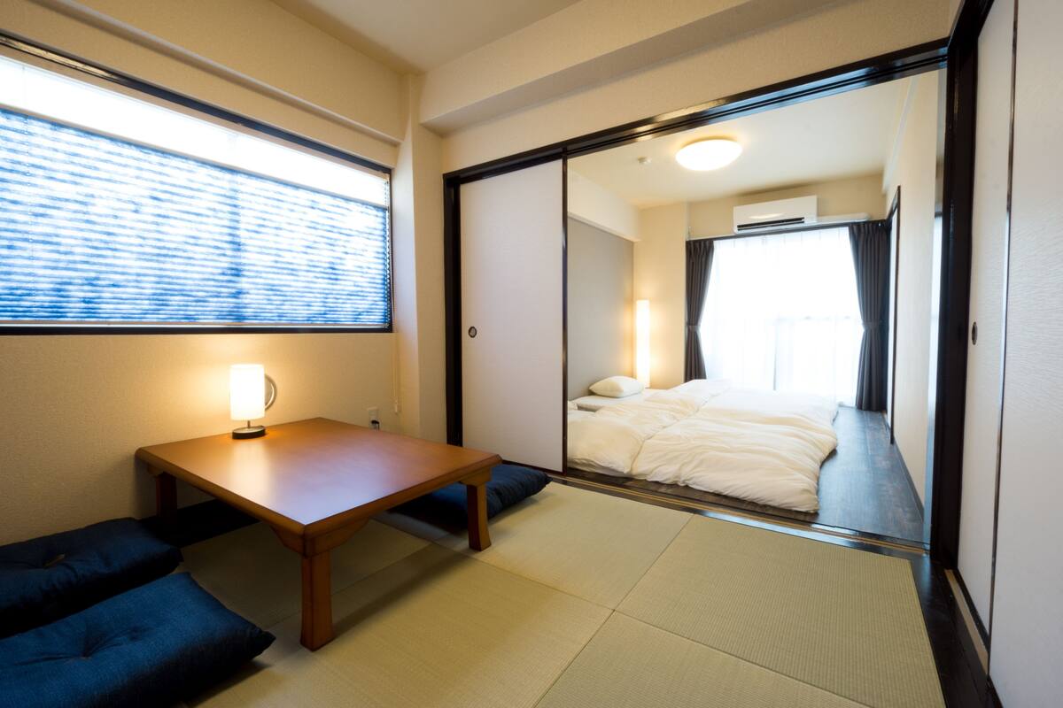 A room with a bed, a table, and a window with blinds.