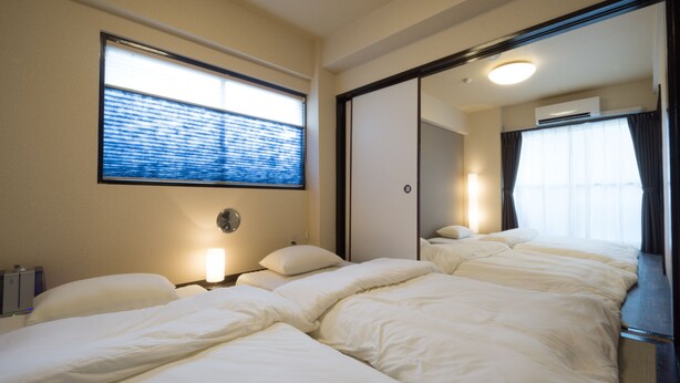 Una habitación de hotel con una cama grande, una mesita de noche, una lámpara, una ventana con persianas y un espejo.