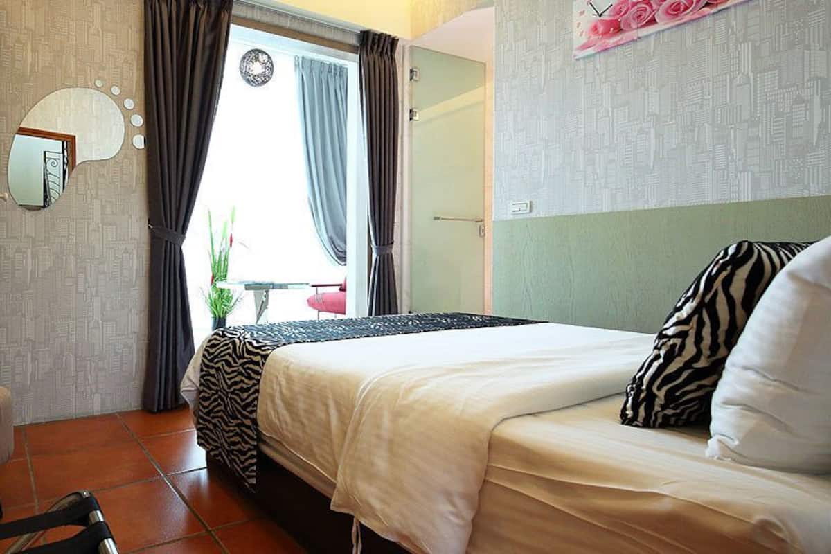 Habitación de hotel con cama, una mesita, una silla, un espejo y una ventana con cortinas.