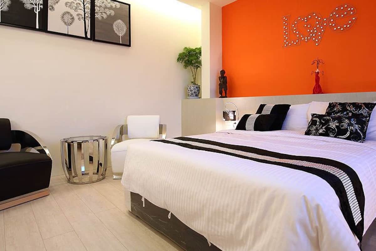 Un dormitorio moderno con una cama grande, una silla negra, una mesita auxiliar pequeña y un elemento decorativo en la pared.